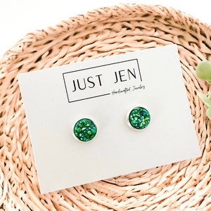 May include: A pair of green glitter stud earrings on a white card with the text "JUST JEN - Handcrafted Jewelry".