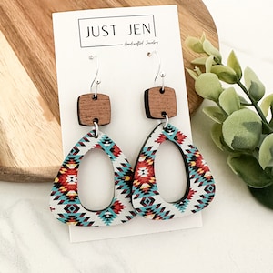 May include: A pair of wooden earrings with a geometric pattern in shades of red, blue, and white. The earrings are shaped like a triangle with a cutout oval in the center. Each earring has a small square wooden piece attached to the top.