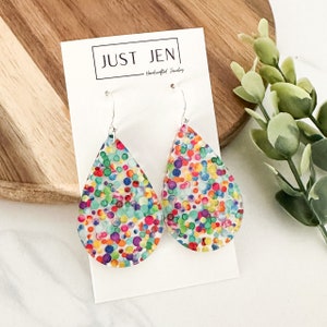 May include: A pair of teardrop-shaped earrings with a colorful confetti pattern. The earrings are made of clear resin and have silver hooks.
