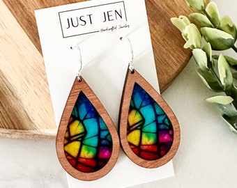 May include: A pair of teardrop-shaped wooden earrings with a rainbow stained glass design. The earrings are handcrafted and have silver hooks.