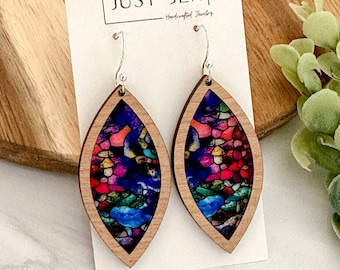 May include: A pair of wooden earrings with a colorful stained glass design. The earrings are shaped like teardrops and have silver hooks.