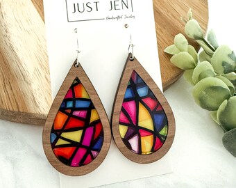 May include: Wooden teardrop earrings with a stained glass design. The earrings feature a colorful mosaic pattern in shades of red, orange, yellow, pink, and blue. The earrings are labeled "JUST JEN - Handcrafted Jewelry".