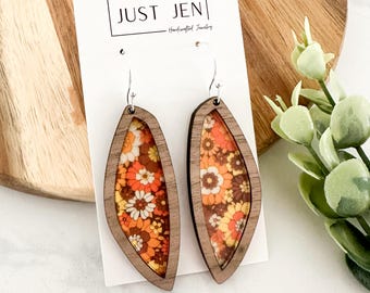 May include: A pair of wooden earrings with a floral pattern inside. The earrings are shaped like a teardrop and have a silver hook.