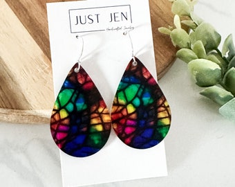 May include: Rainbow stained glass teardrop earrings with silver hooks. The earrings are handmade and feature a colorful abstract design.