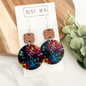 May include: A pair of colorful floral earrings with a wood accent. The earrings are made of wood and have a round shape with a floral design. The earrings are hanging from silver hooks.