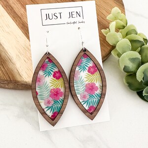 May include: A pair of wooden earrings with a floral print. The earrings are shaped like a teardrop and have a silver hook.