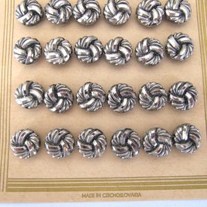 May include: A sheet of silver metal buttons with a knotted design. The buttons are arranged in rows on a card with the text "MADE IN CZECHOSLOVAKIA".