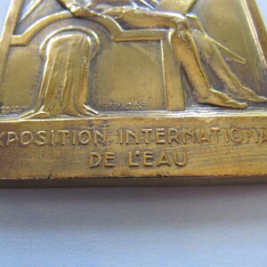 K&ouml;nnte beinhalten: Eine Bronzemedaille mit einem Relief einer sitzenden Figur. Die Medaille ist mit "Exposition Internationale de L'Eau" beschriftet.