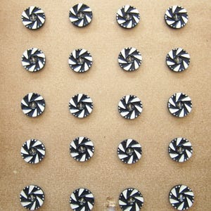 Peut inclure: Une feuille de papier brun avec 16 boutons noirs et blancs disposés en grille. Les boutons ont un motif en spirale.