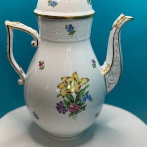 May include: White porcelain coffee pot with a floral design. The pot features a yellow, red, and purple flower bouquet on the front, with smaller floral accents. The lid is topped with a yellow rose and gold trim.
