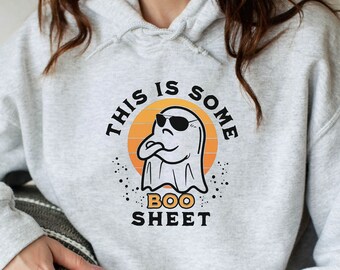 May include: Light gray hoodie with a graphic of a ghost wearing sunglasses and the text "THIS IS SOME BOO SHEET". The ghost is in front of an orange and yellow sunset. The hoodie is a pullover style.