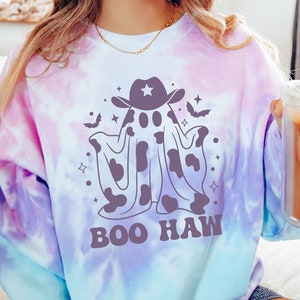 May include: A tie-dye sweatshirt with a purple, blue, and white color scheme. The sweatshirt features a cartoon ghost wearing a cowboy hat and the text "BOO HAW".