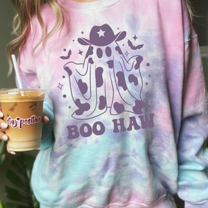 May include: A tie-dye sweatshirt with a purple ghost wearing a cowboy hat and the text "BOO HAW" in purple. The ghost has a cow print pattern.