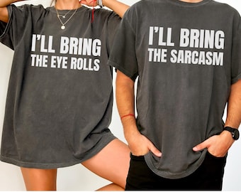 May include: Two dark gray t-shirts with white text. One shirt reads "I'LL BRING THE EYE ROLLS," and the other says "I'LL BRING THE SARCASM." The shirts have short sleeves and a relaxed fit, suitable for casual wear.