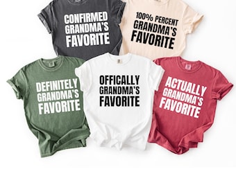 May include: Five short-sleeve crew neck t-shirts in charcoal, cream, olive green, white, and red. Each shirt features bold text: CONFIRMED GRANDMA'S FAVORITE, 100% PERCENT GRANDMA'S FAVORITE, DEFINITELY GRANDMA'S FAVORITE, OFFICIALLY GRANDMA'S FAVORITE, and ACTUALLY GRANDMA'S FAVORITE.