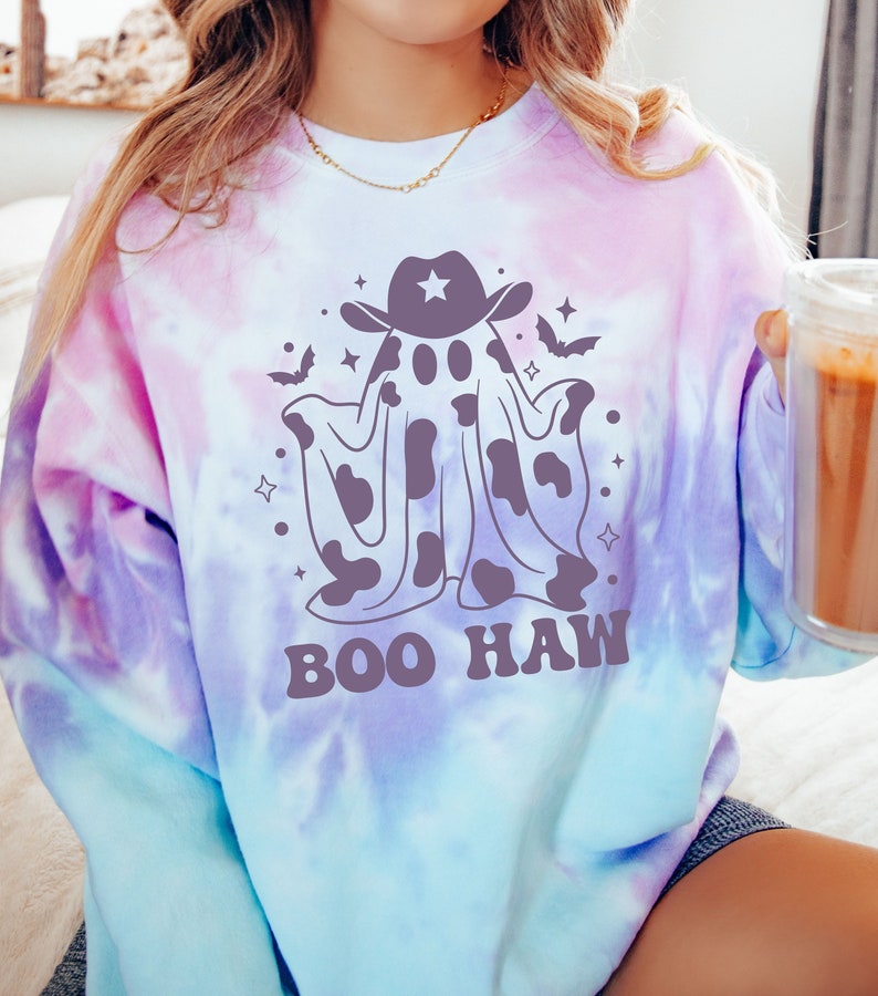 May include: A tie-dye sweatshirt with a purple, blue, and white color scheme. The sweatshirt features a cartoon ghost wearing a cowboy hat and the text "BOO HAW".