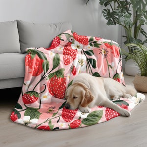 Może przedstawiać: R&oacute;żowo-zielony koc z wzorem truskawek i kwiat&oacute;w. Na kocu leży golden retriever.