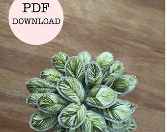 Può includere: Primo piano di un fiore di stoffa ricamato in verde e bianco. Il fiore è composto da molte piccole foglie cucite insieme.