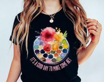 May include: A black t-shirt with a watercolor design of a paint palette with flowers and the text "It's a good day to make some art".