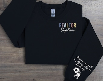 May include: Black sweatshirt with the text "REALTOR Sophia" on the front and "Home is not a place, it's a feeling" with a house and keys on the sleeve.