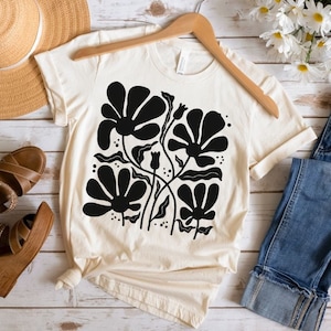 May include: A white t-shirt with a black floral design. The design features stylized flowers with rounded petals and stems.
