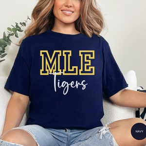 May include: A navy blue t-shirt with the text "MLE Tigers" in yellow and white lettering. The shirt is made of a soft, comfortable material.