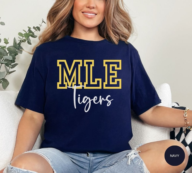 May include: A navy blue t-shirt with the text "MLE Tigers" in yellow and white lettering. The shirt is made of a soft, comfortable material.