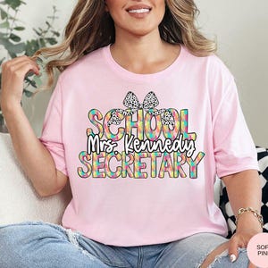Może przedstawiać: R&oacute;żowa koszulka z tęczowym i czarno-białym wzorem w kropki z napisem "School Mrs. Kennedy Secretary".