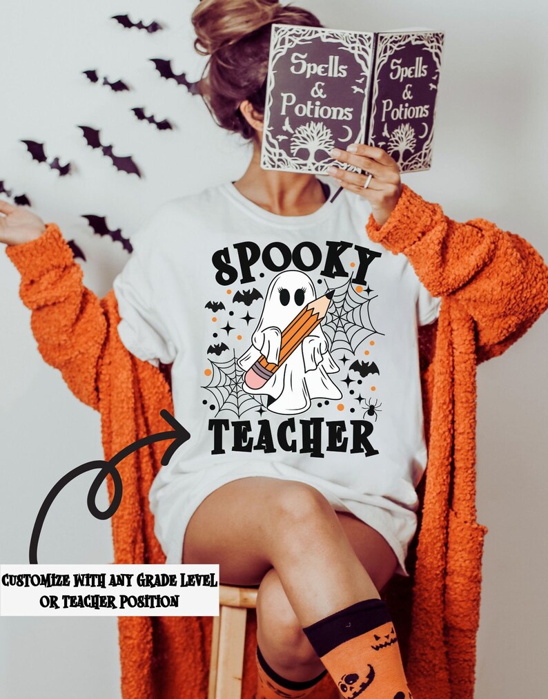 May include: White t-shirt with a spooky ghost holding a pencil and the text "Spooky Teacher". The ghost is surrounded by bats, spiderwebs, and stars. The text "Customize with any grade level or teacher position" is at the bottom of the image.