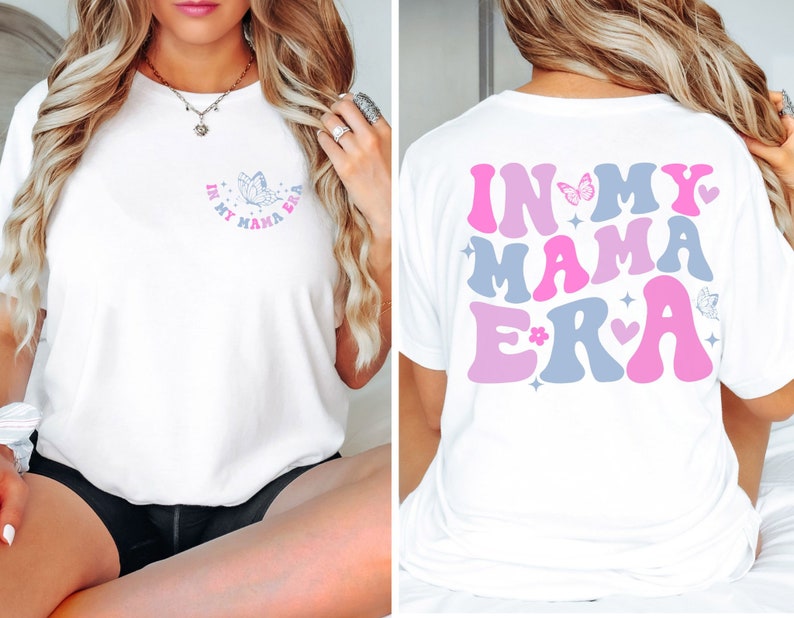 May include: White t-shirt with the text "In My Mama Era" in pink, blue, and white letters with a butterfly and hearts. The text is in a retro font.