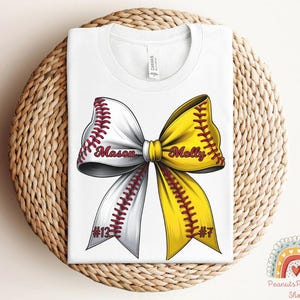 May include: White t-shirt with a yellow and white softball bow with red stitching. The bow has the names "Mason" and "Molly" written on it, and the numbers "#13" and "#7" on the bottom.