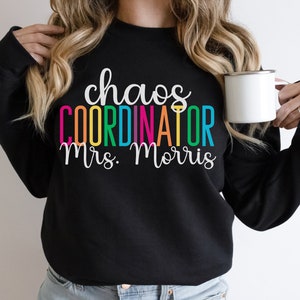 Pu&ograve; includere: Felpa nera con il testo "chaos coordinator Mrs. Morris" in colori arcobaleno.