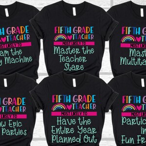 K&ouml;nnte beinhalten: Sechs schwarze T-Shirts mit einem Regenbogen- und Herzdesign. Jedes Shirt tr&auml;gt den Schriftzug "Fifth Grade Teacher" und darunter einen anderen Spruch. Die Spr&uuml;che lauten: "Most Likely To Jam the Copy Machine", "Most Likely To Master the Teacher Stare", "Most Likely To Master Multitasking", "Most Likely To Throw Epic Class Parties", "Most Likely To Have the Entire Year Planned Out" und "Most Likely To Participate in Fun Fridays".