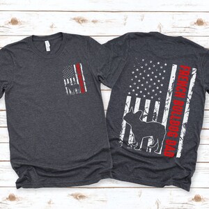 May include: Two dark heather grey t-shirts with a distressed American flag design. The front shirt has a small French Bulldog silhouette on the flag. The back shirt has a larger French Bulldog silhouette and the text "French Bulldog Dad" on the flag.