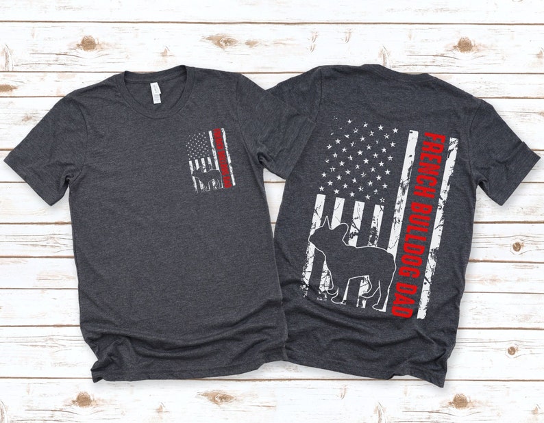 May include: Two dark heather grey t-shirts with a distressed American flag design. The front shirt has a small French Bulldog silhouette on the flag. The back shirt has a larger French Bulldog silhouette and the text "French Bulldog Dad" on the flag.