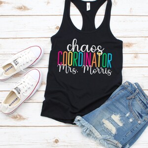 Pu&ograve; includere: Canotta nera con la scritta "chaos coordinator Mrs. Morris" in colori arcobaleno. Il testo &egrave; in un font divertente. La canotta &egrave; indossata con pantaloncini di jeans e scarpe da ginnastica bianche.