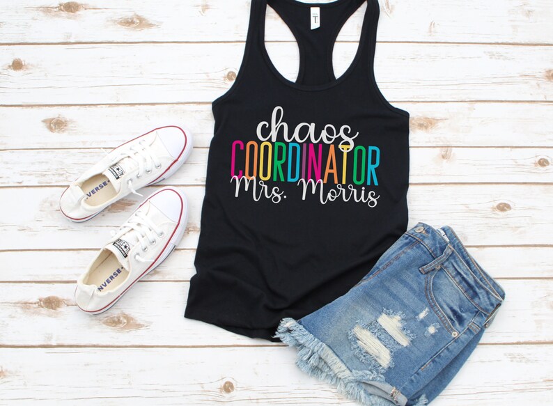 Pu&ograve; includere: Canotta nera con la scritta "chaos coordinator Mrs. Morris" in colori arcobaleno. Il testo &egrave; in un font divertente. La canotta &egrave; indossata con pantaloncini di jeans e scarpe da ginnastica bianche.