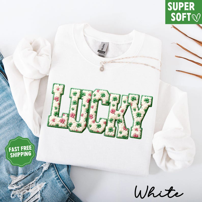 Pu&ograve; includere: Felpa bianca con la scritta "LUCKY" ricamata in verde e crema con motivo floreale. La felpa ha girocollo e maniche lunghe. Una collana d'argento con un piccolo ciondolo &egrave; sulla maglia. Sono visibili anche le parole "SUPER SOFT" e "White".