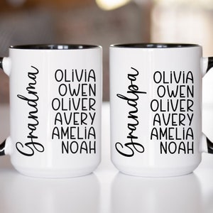 May include: Two white ceramic mugs with black rims and handles. The mugs have black text that reads "Grandma" and "Grandpa" with a list of names underneath: Olivia, Owen, Oliver, Avery, Amelia, Noah.