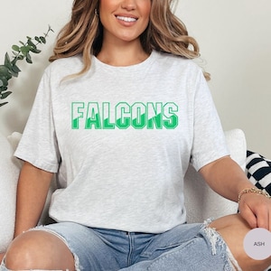 May include: A heather grey t-shirt with the word "FALCONS" printed in green letters. The letters have a white outline.