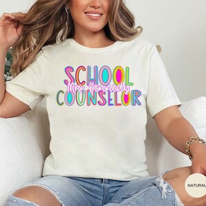 May include: A white t-shirt with the text "SCHOOL COUNSELOR" in colorful letters. The text "Mrs. Kennedy" is written in smaller letters below the main text.