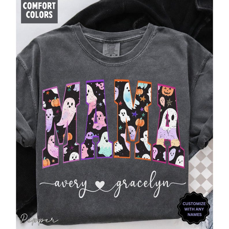May include: Dark gray t-shirt with the word "MAMA" in colorful letters filled with ghost and pumpkin graphics. The names "avery" and "gracelyn" are written below the word "MAMA". The shirt has the text "CUSTOMIZE WITH ANY NAMES".