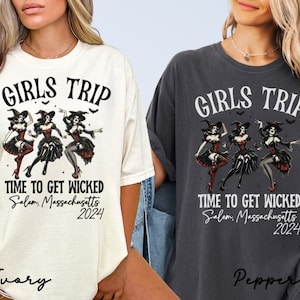 May include: Two women wearing t-shirts with a graphic of three witches dancing. The text on the shirts reads "Girls Trip" and "Time to Get Wicked Salem, Massachusetts 2024". One shirt is ivory and the other is pepper.