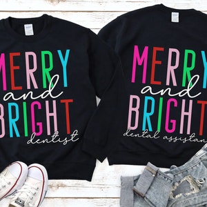 May include: Two black sweatshirts with the text "Merry and Bright" in colorful letters. One sweatshirt says "dentist" and the other says "dental assistant".