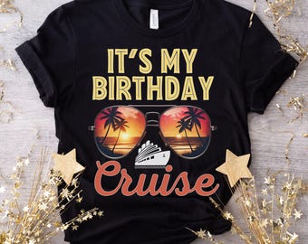 Puede incluir: Camiseta negra con el texto "It's My Birthday Cruise" en amarillo y naranja. El texto está rodeado por unas gafas de sol con una puesta de sol y palmeras reflejadas en las lentes. Se puede ver un crucero en las gafas de sol.