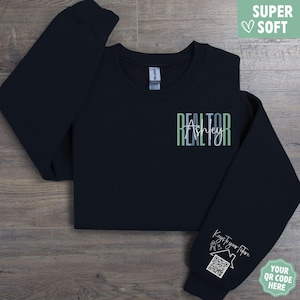 May include: A navy blue sweatshirt with the word "REALTOR" in green and white, with the name "Ashley" below it. The sleeve has the text "Keys to your future" and a QR code. The words "SUPER SOFT" are in a green box.