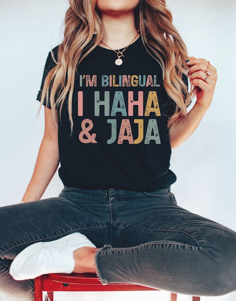 Puede incluir: Una camiseta negra con el texto "I'm Bilingual I HAHA & Jaja" en letras de colores desgastadas. El texto est&aacute; en una fuente de estilo vintage.
