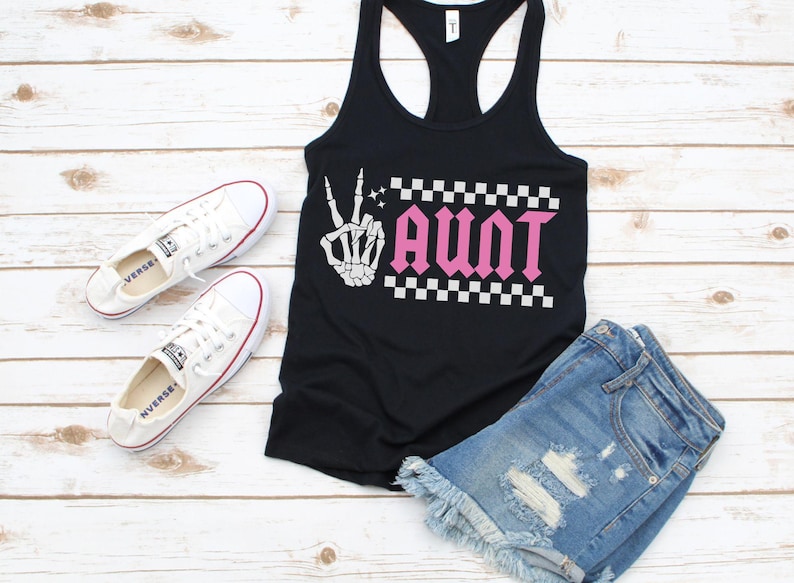 K&ouml;nnte beinhalten: Schwarzes Tanktop mit einer wei&szlig;en Skeletthand, die ein Peacezeichen macht, und dem Wort "AUNT" in rosa Buchstaben mit einem karierten Muster dahinter.