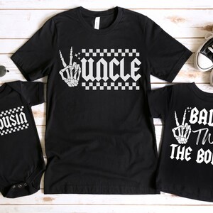 May include: Three black t-shirts with white text and graphics. The shirts say "Uncle", "Cousin", and "Bad Two The Bone".
