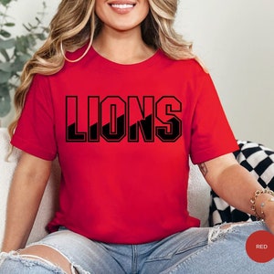 May include: A red t-shirt with the word "LIONS" printed in black block letters. The letters have a diagonal black stripe through them.